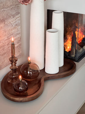 Complete woonset Walnut en Warmth met drie witte Cone vazen, een organisch houten Villeta walnut dienblad en drie brandende Peri Living olielampjes op een modern dressoir. Shop the Look