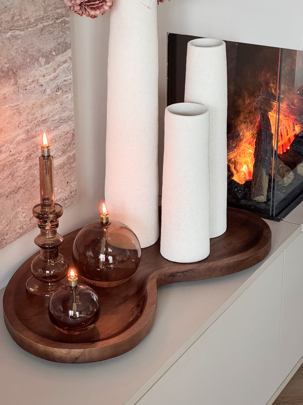 Complete woonset Walnut en Warmth met drie witte Cone vazen, een organisch houten Villeta walnut dienblad en drie brandende Peri Living olielampjes op een modern dressoir. Shop the Look