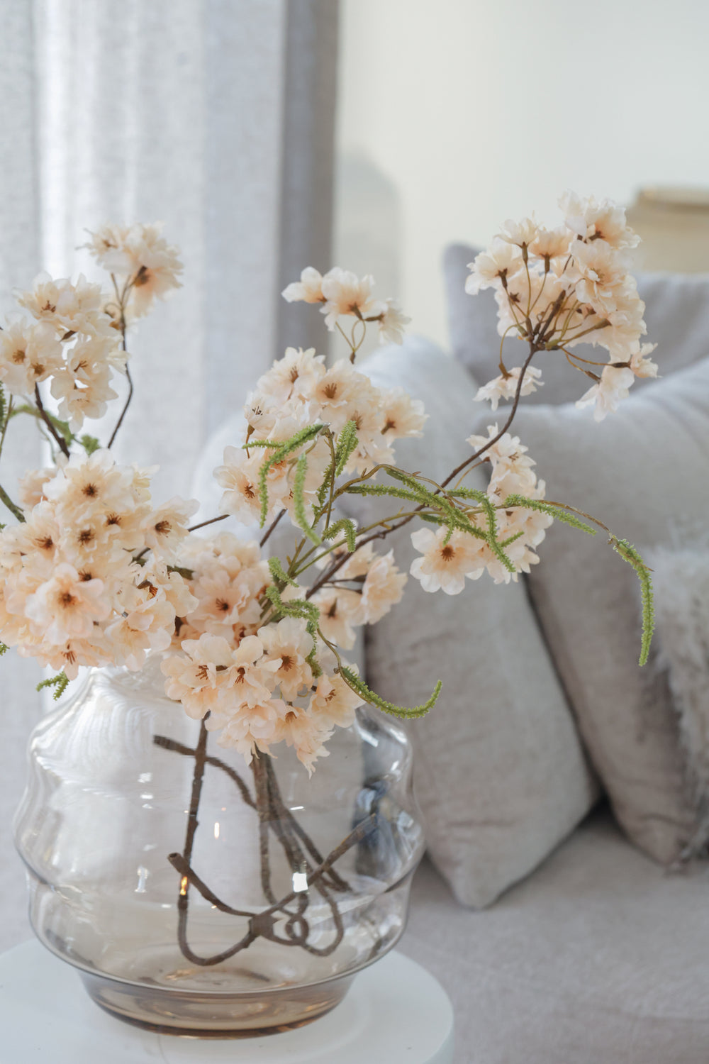 Glazen designvaas met soft peachkleurige kunstbloesemtakken voor een luxe en onderhoudsvrij Hotel Chic interieur.
