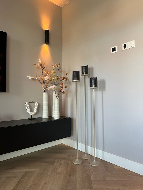 Set van 3 matbeige stalen Onah vloerkandelaren in verschillende hoogtes (100 cm, 110 cm en 120 cm) met zwarte PTMD LED-kaarsen.